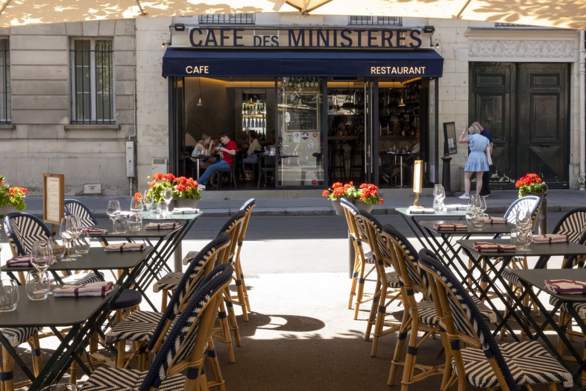 Café des Ministères exterior terrace with striped chairs, red flowers and the restaurant's awning sign
