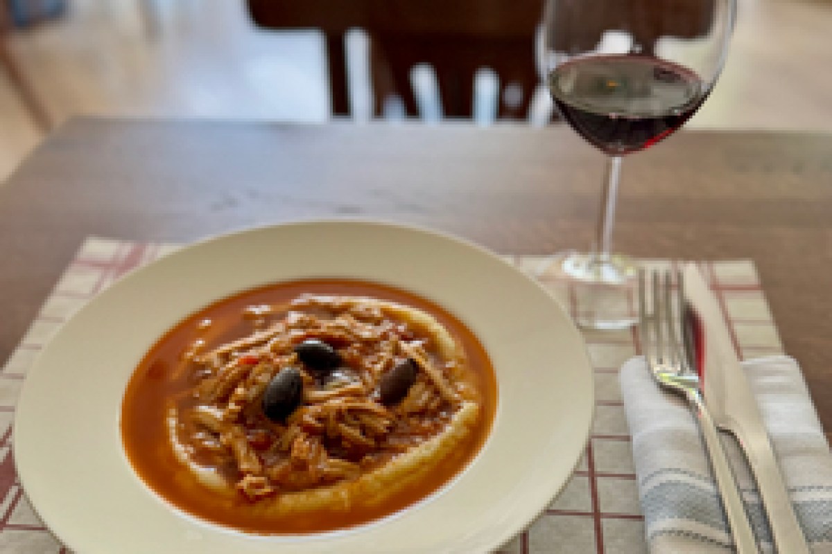 A pasta dish topped with olives in tomato sauce, served with a glass of red wine on a set table