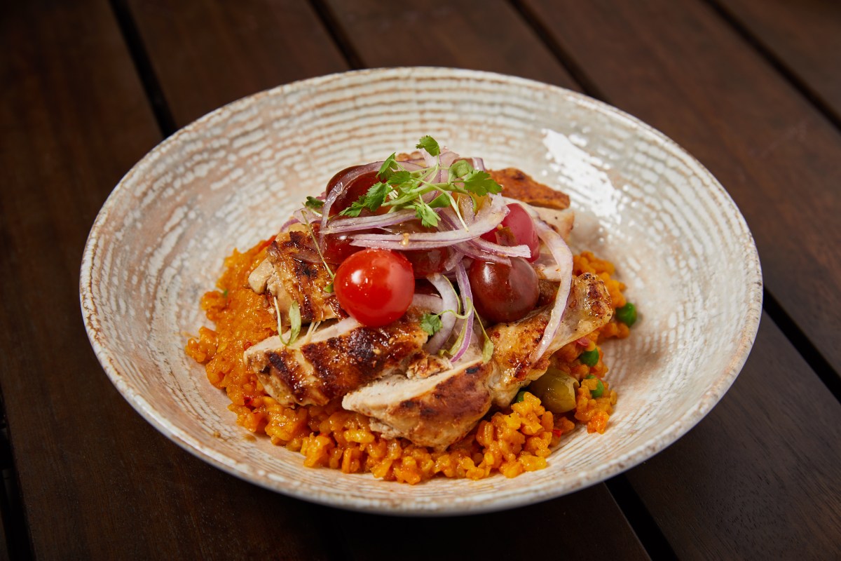 Bowl of yellow rice with grilled chicken, cherry tomatoes and red onion on wooden table