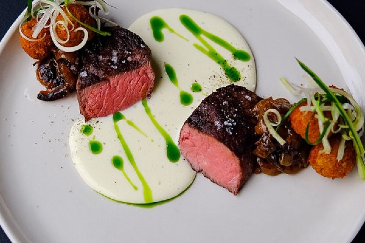 Plated seared steak slices with cauliflower cream, herb oil drizzle, and fried bites