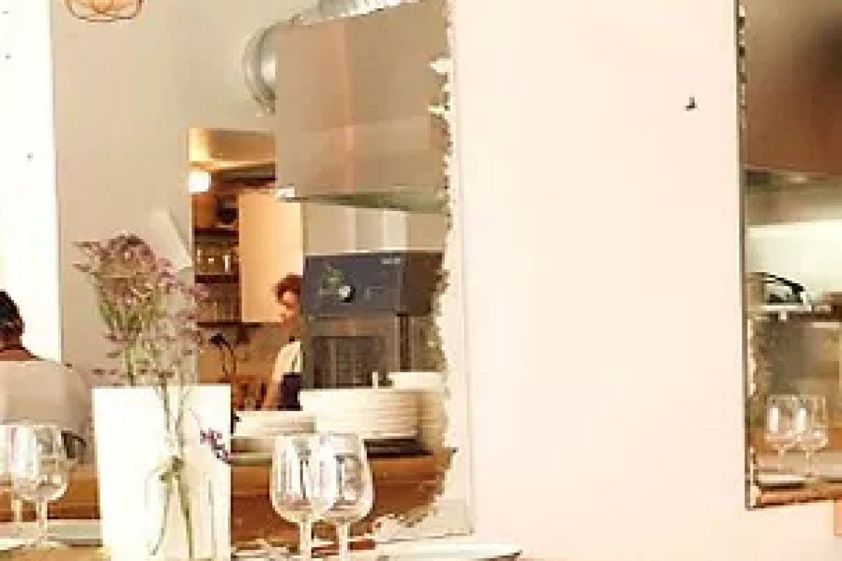 Laid table with wine glasses and a small flower vase, kitchen pass visible in mirror behind