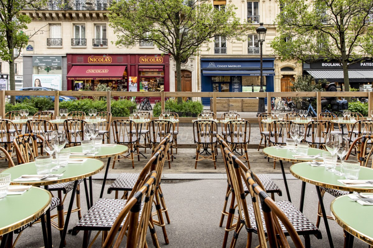 Outdoor terrace with green bistro tables and rattan chairs set along a Paris street lined with shops