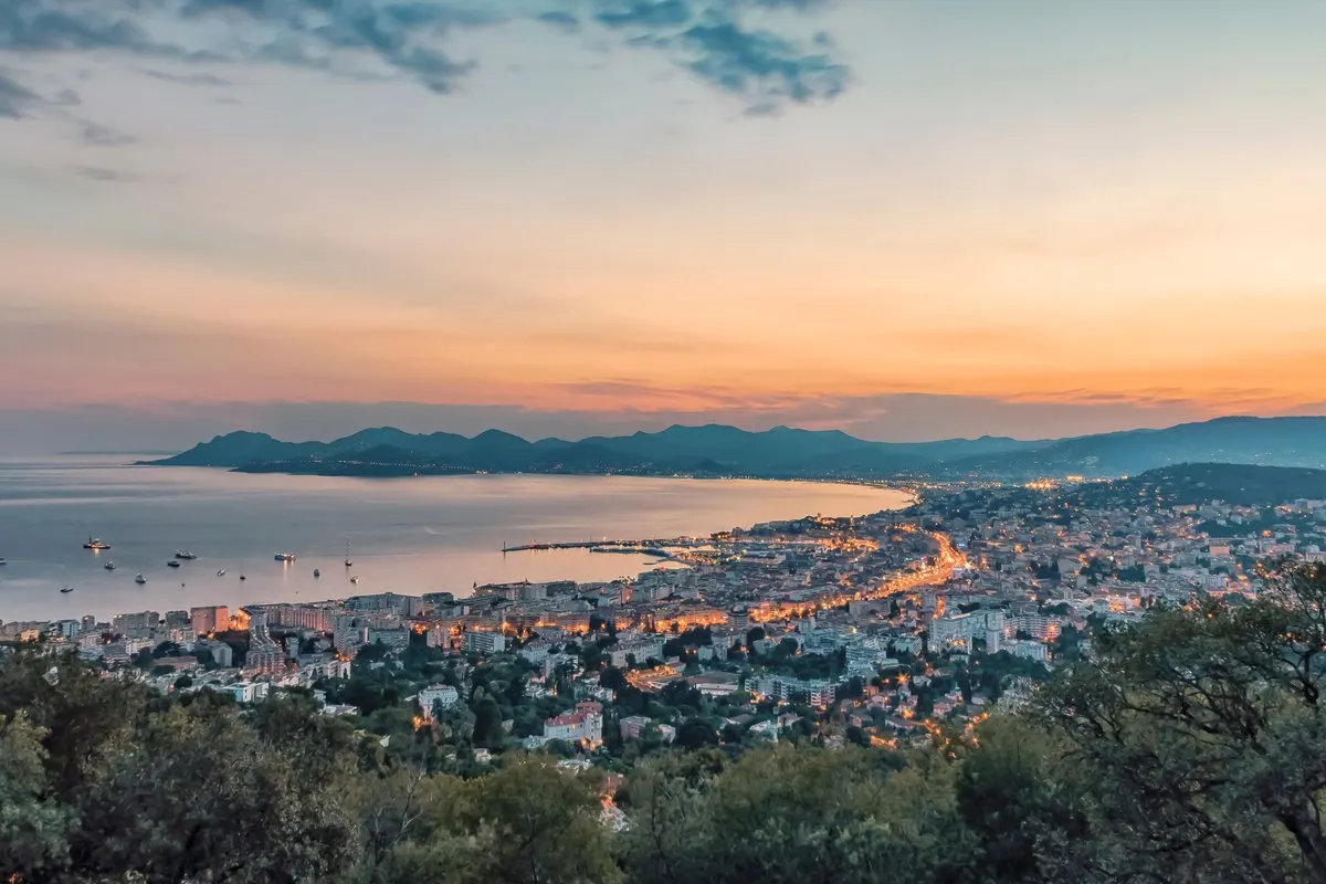Cannes and the bay at dusk seen from above, with the illuminated coastline of La Croisette and the mountains in the distance