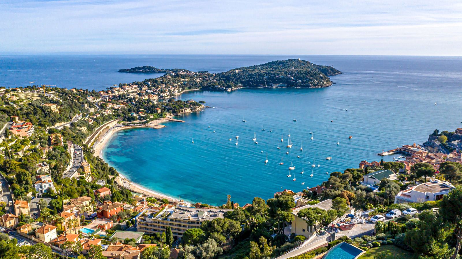 The Cap Ferrat peninsula and a turquoise bay with moored sailing boats, seen from the heights above the coast