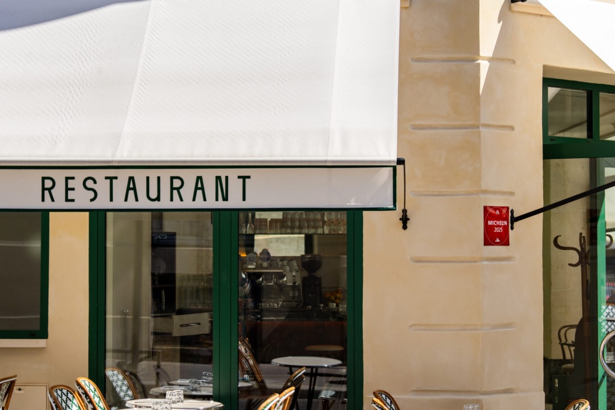 Exterior of Capsule restaurant with white awning reading 'RESTAURANT', Michelin 2025 plaque, and outdoor terrace tables.
