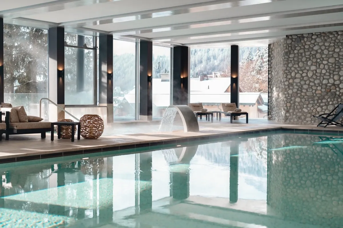 Indoor hotel pool with stone wall, loungers and snowy village view through windows
