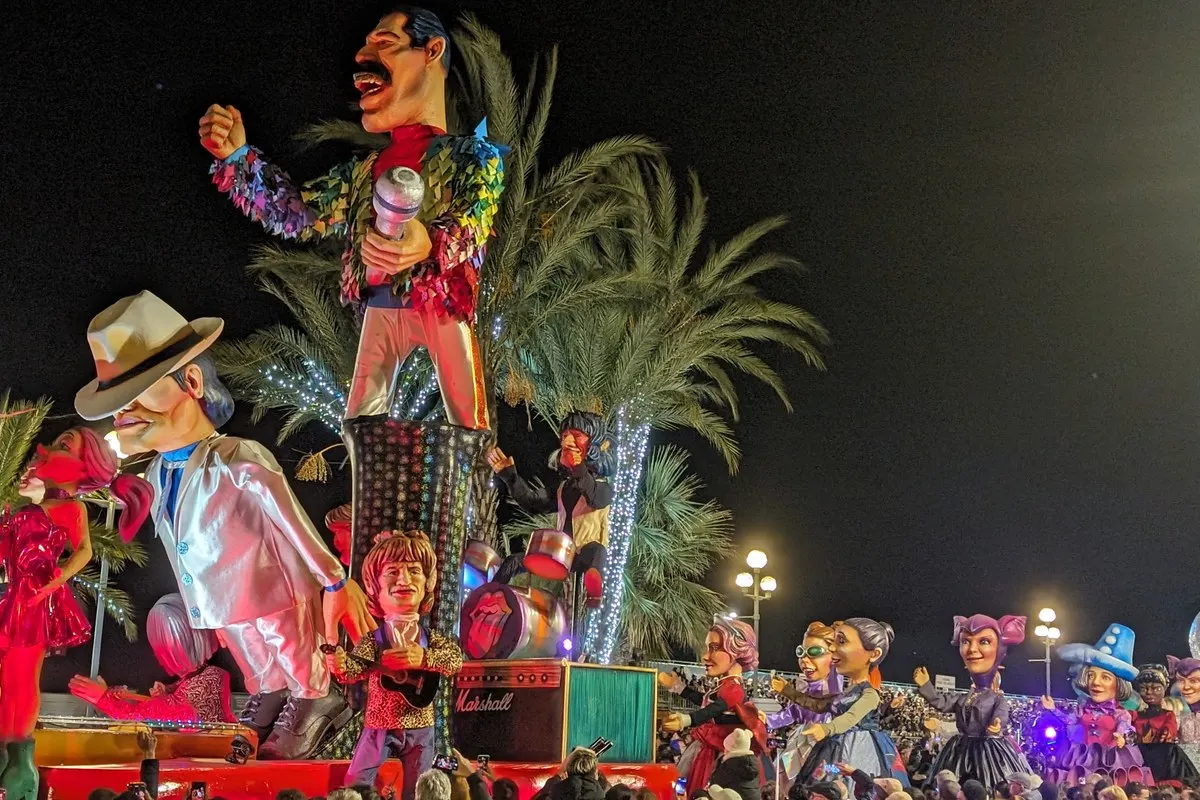 Giant illuminated carnival floats with caricature figures parading at night during the Carnival of Nice