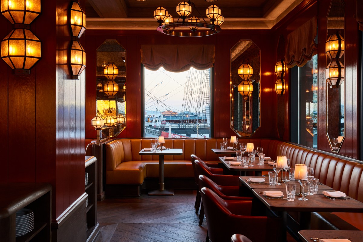 Dining room with red walls, leather booths, lanterns, and harbor view through window.