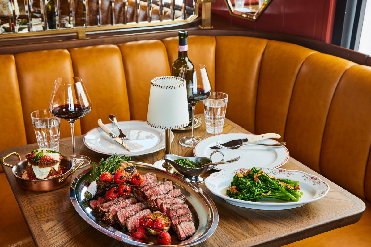 Table set with steak platter, broccoli rabe, mozzarella dish, wine and glasses.