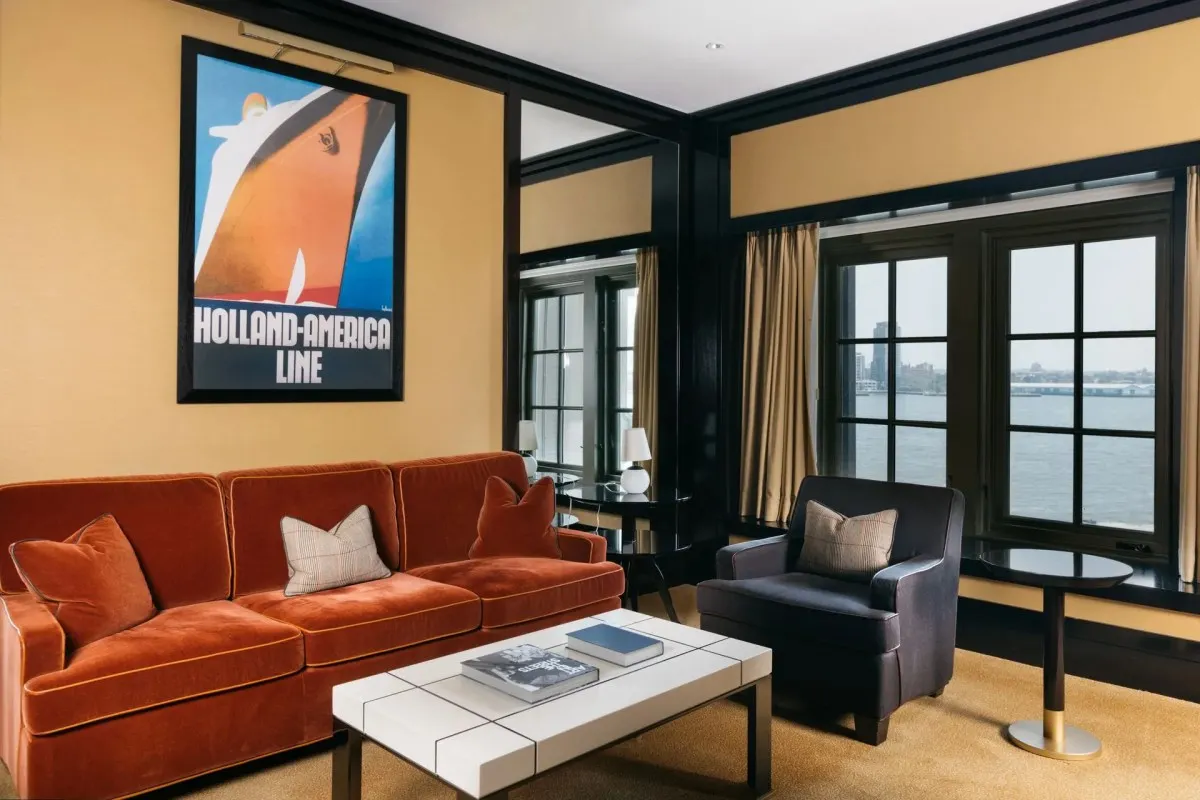 Suite living room with vintage ocean liner poster, orange sofa, and harbor view windows