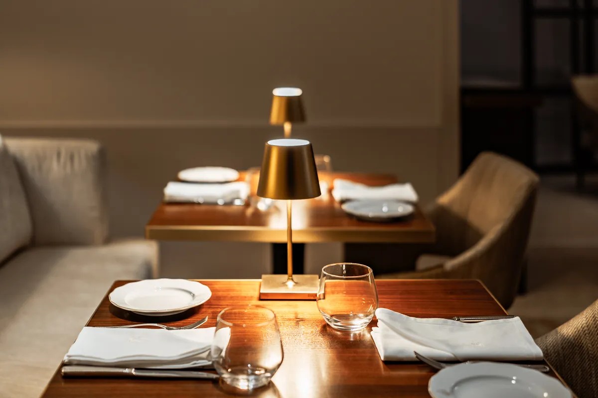 Elegant restaurant interior with set tables, wine glasses and warm lamp lighting.