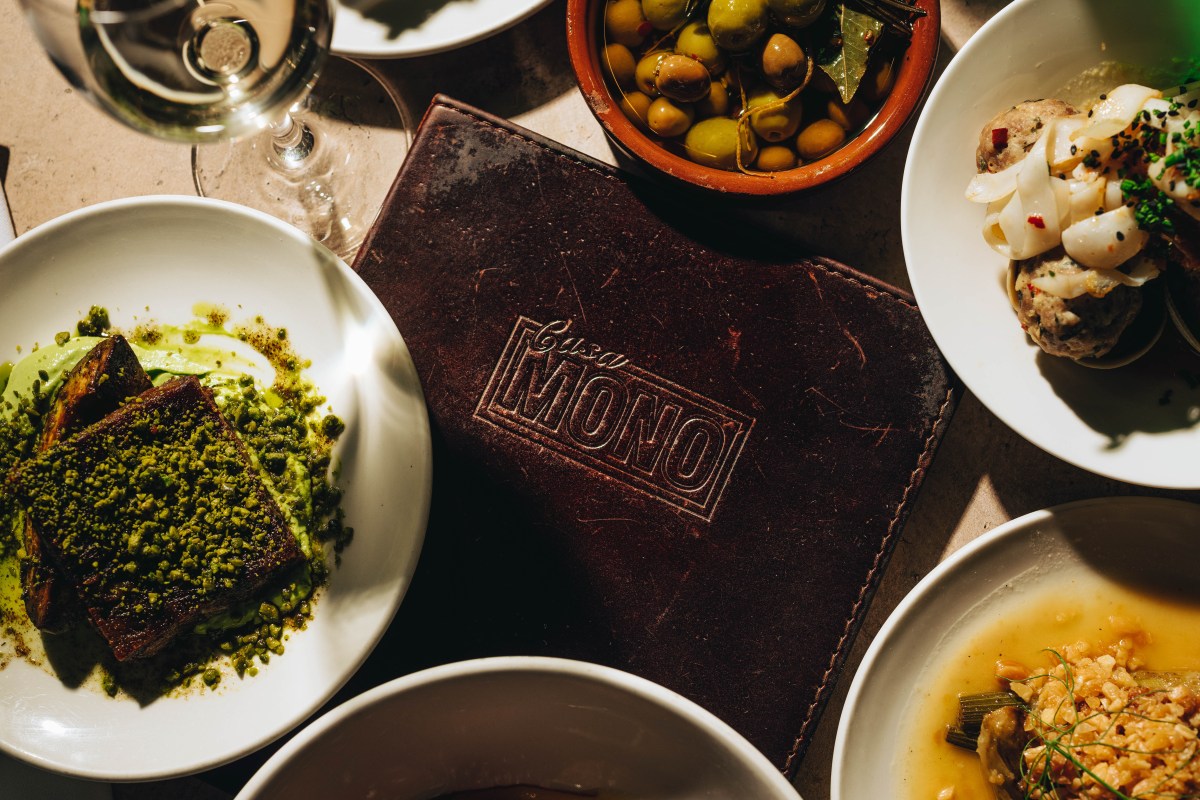 Overhead shot of a laid table with Casa Mono leather menu, olives, pork belly dish, and tapas plates