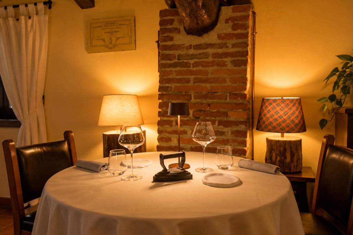 Cozy table setting near a brick fireplace with warm lamps and wine glasses.