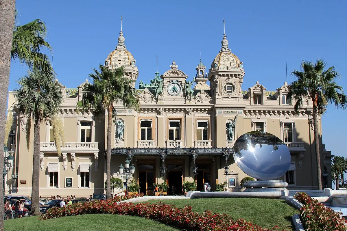 The Belle Époque façade of the Casino de Monte-Carlo with its twin towers, palms and a mirrored sculpture in front