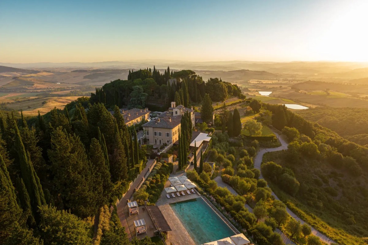 Aerial view of the hillside hotel estate with pool, gardens, and Tuscan countryside at sunset.