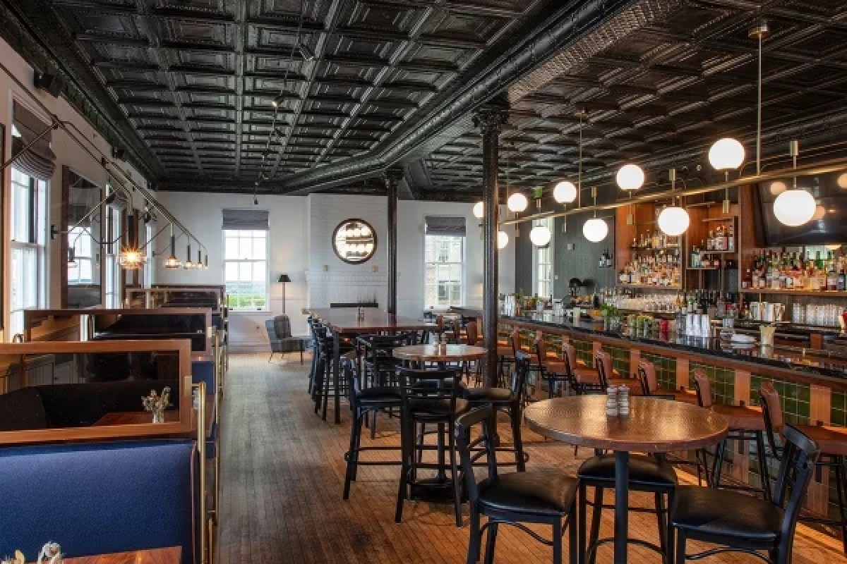 Cozy hotel bar/lounge with tin ceiling, wood floors, booth seating and backlit bottle shelves