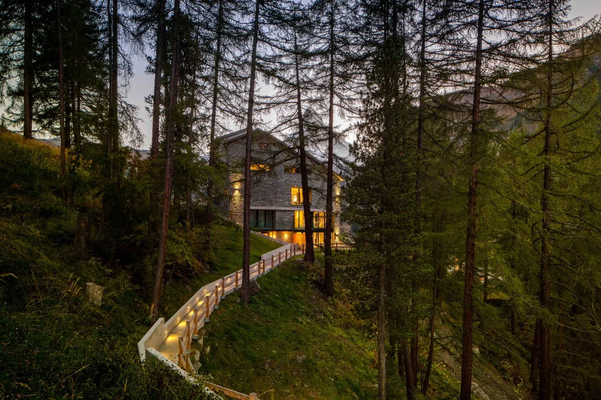 Stone-and-wood CERVO Mountain Resort building glowing with warm lights at dusk, surrounded by tall pine trees and a lit pathway