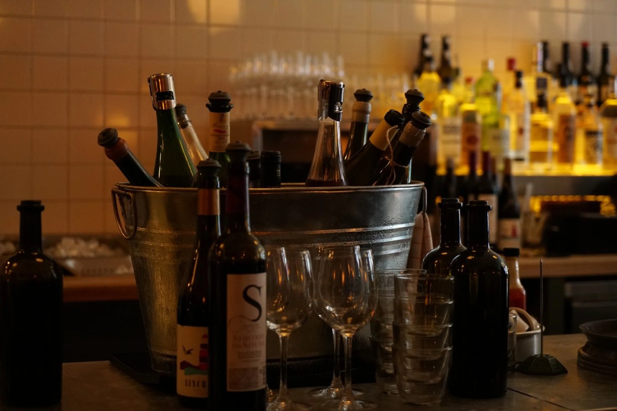 Bar counter with wine bottles in an ice bucket and glasses, shelves of liquor bottles in background