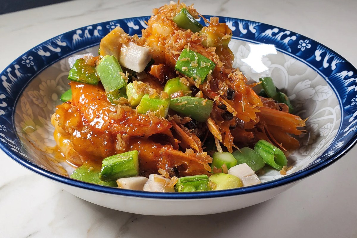 Bowl of saucy shrimp with crispy shallots and green vegetables on patterned plate