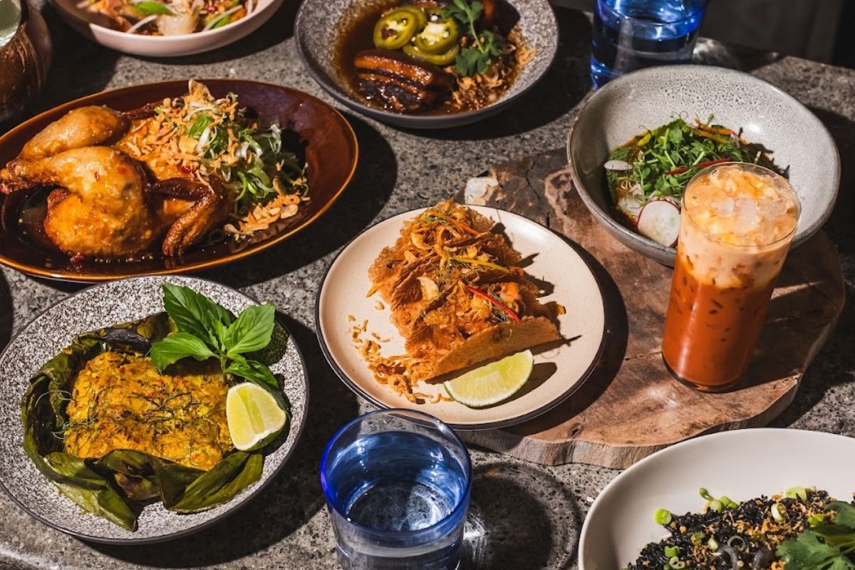 Spread of Thai dishes on table including roasted chicken, crispy fish, curry, salad and a Thai iced tea