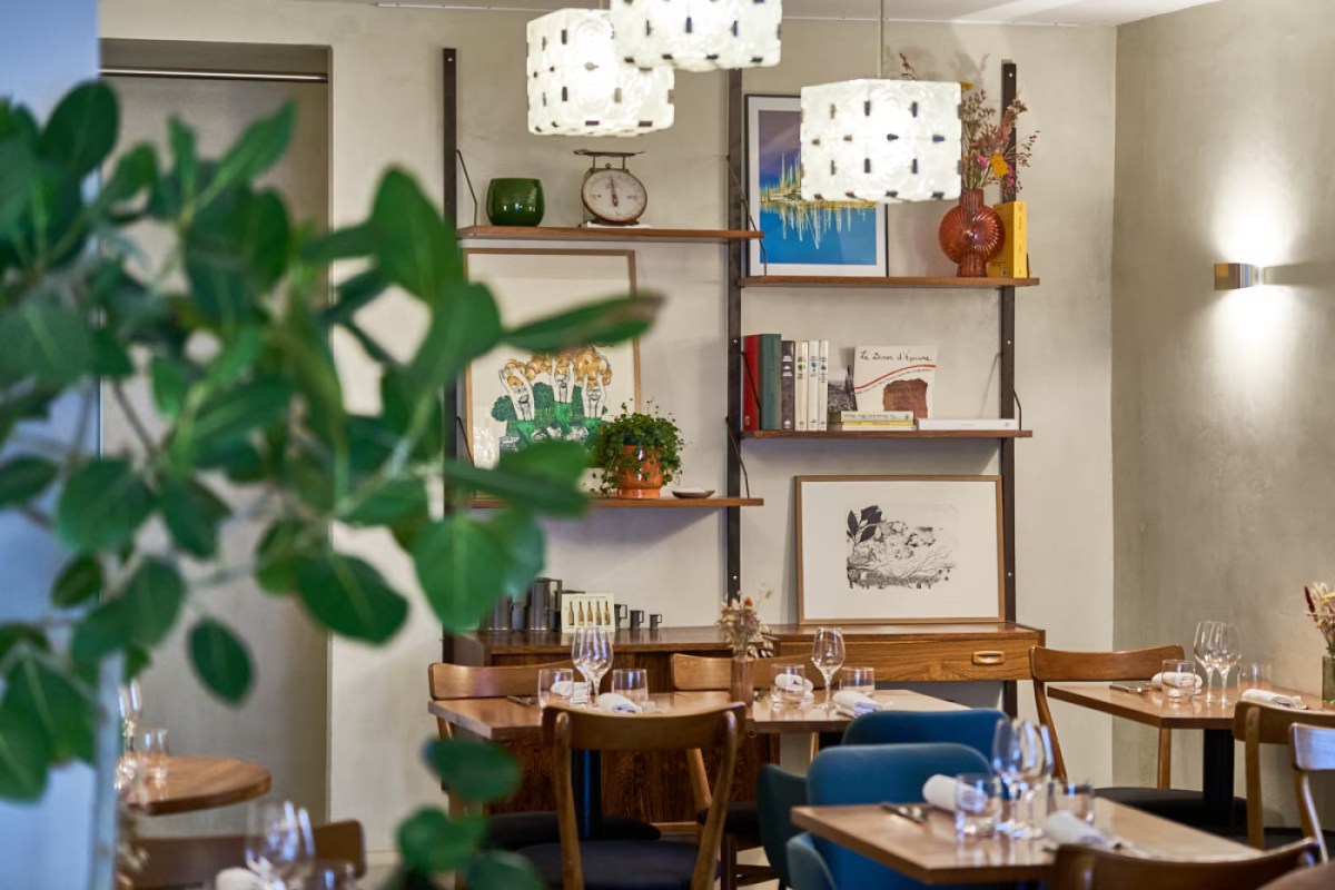 Restaurant dining room with wooden tables, blue chairs, shelving with books and decor, pendant lights