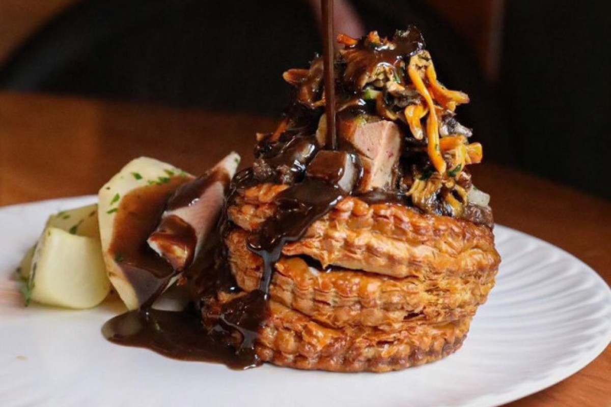 Plated dish with pastry, meat, mushrooms, and dark sauce drizzled on top