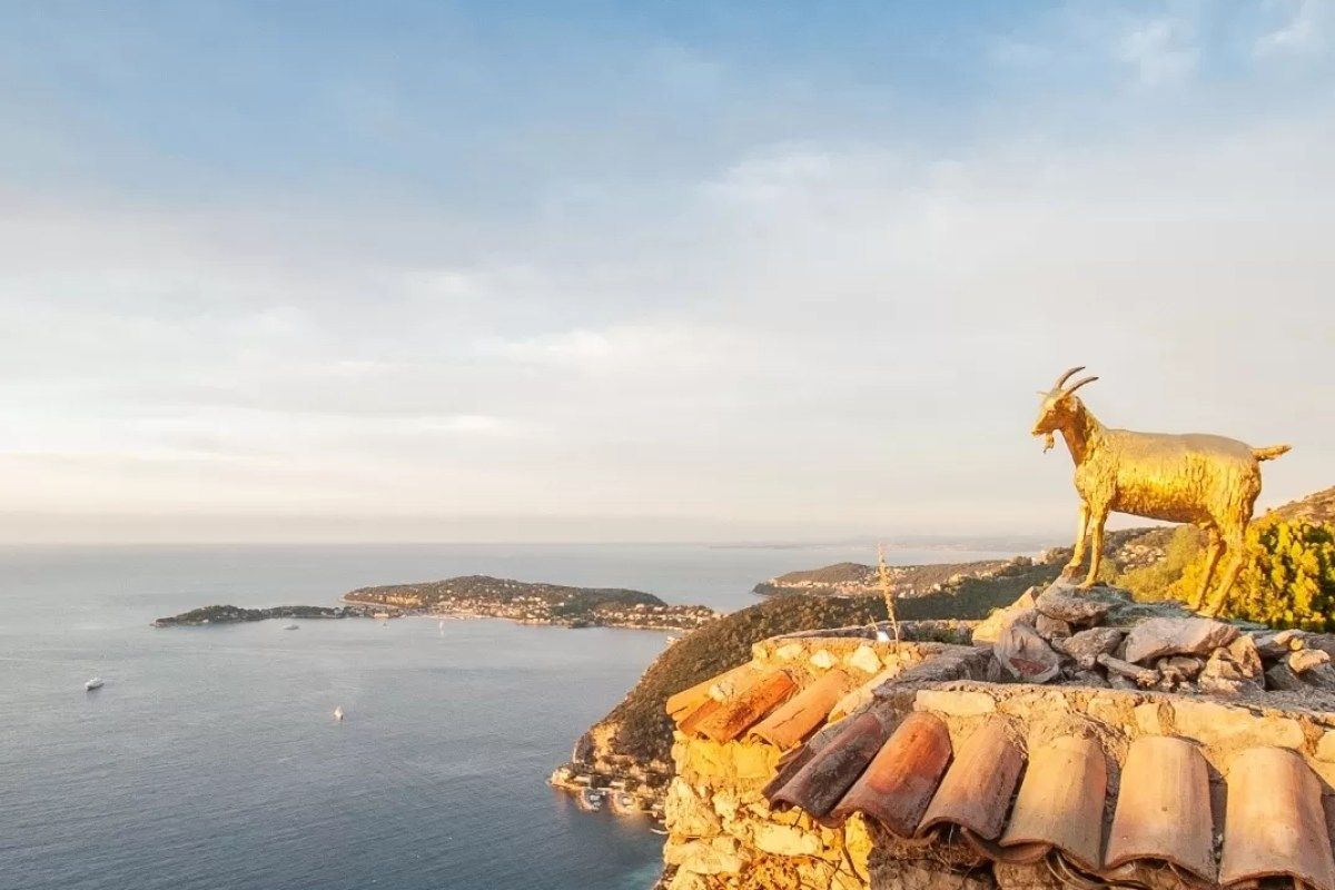 Golden goat statue on a rooftop with panoramic Mediterranean coastal view at sunset