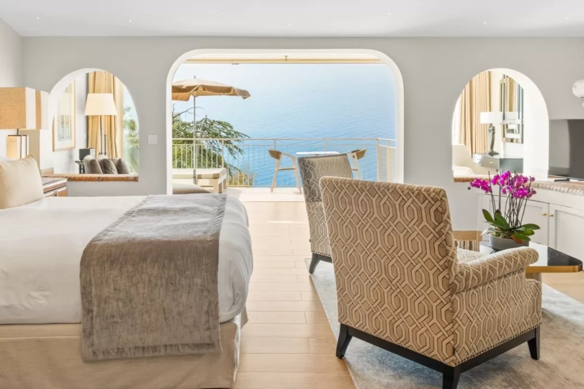 Hotel suite bedroom with archways opening to a sea-view balcony and modern furnishings