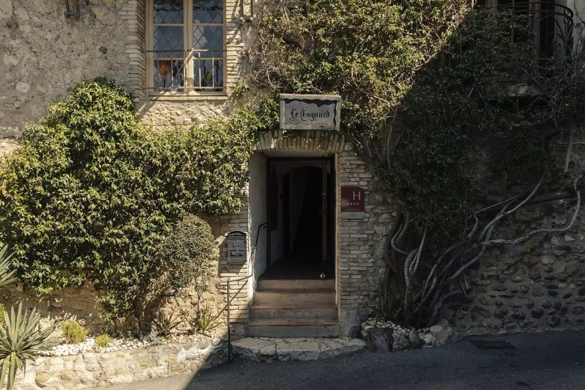 Stone building entrance with ivy and sign reading 'Le Cagnard', the hotel's exterior facade