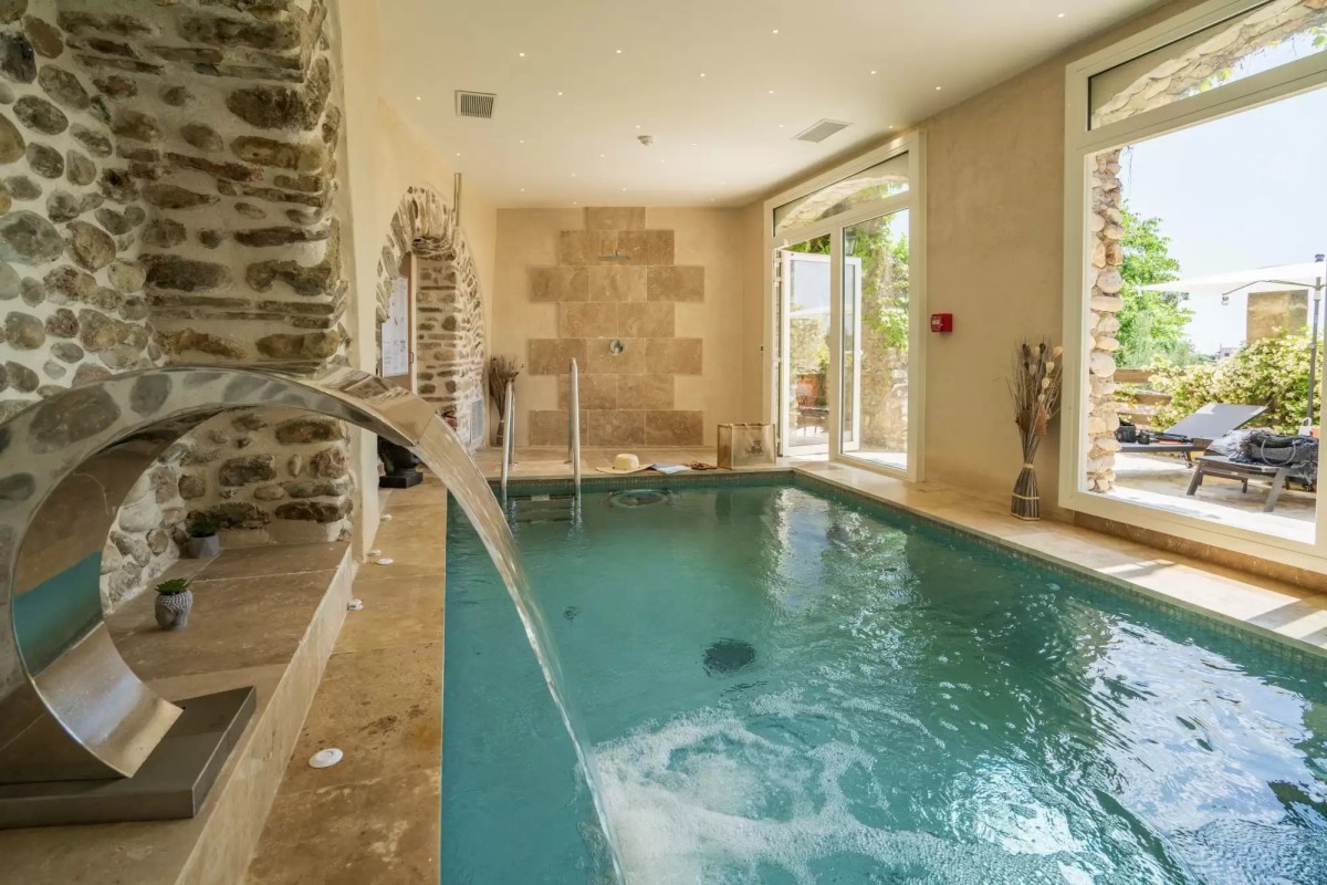 Indoor spa pool with stone walls, water feature, and glass doors opening to a terrace