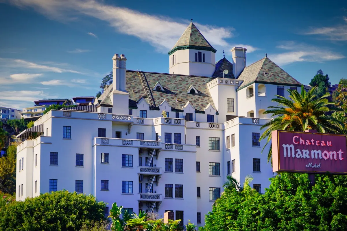 White castle-like Chateau Marmont hotel building with tower, palm tree and hotel sign, blue sky