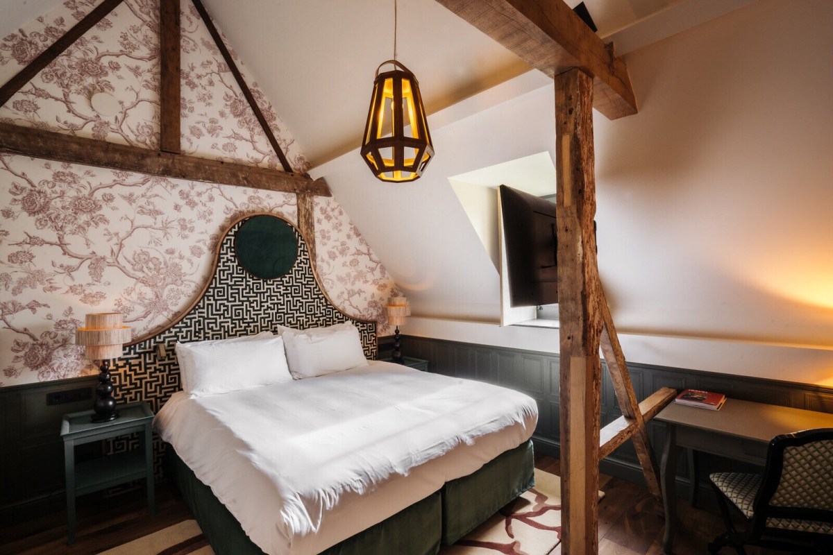 Cozy attic guest room with exposed beams, patterned headboard, and floral wallpaper