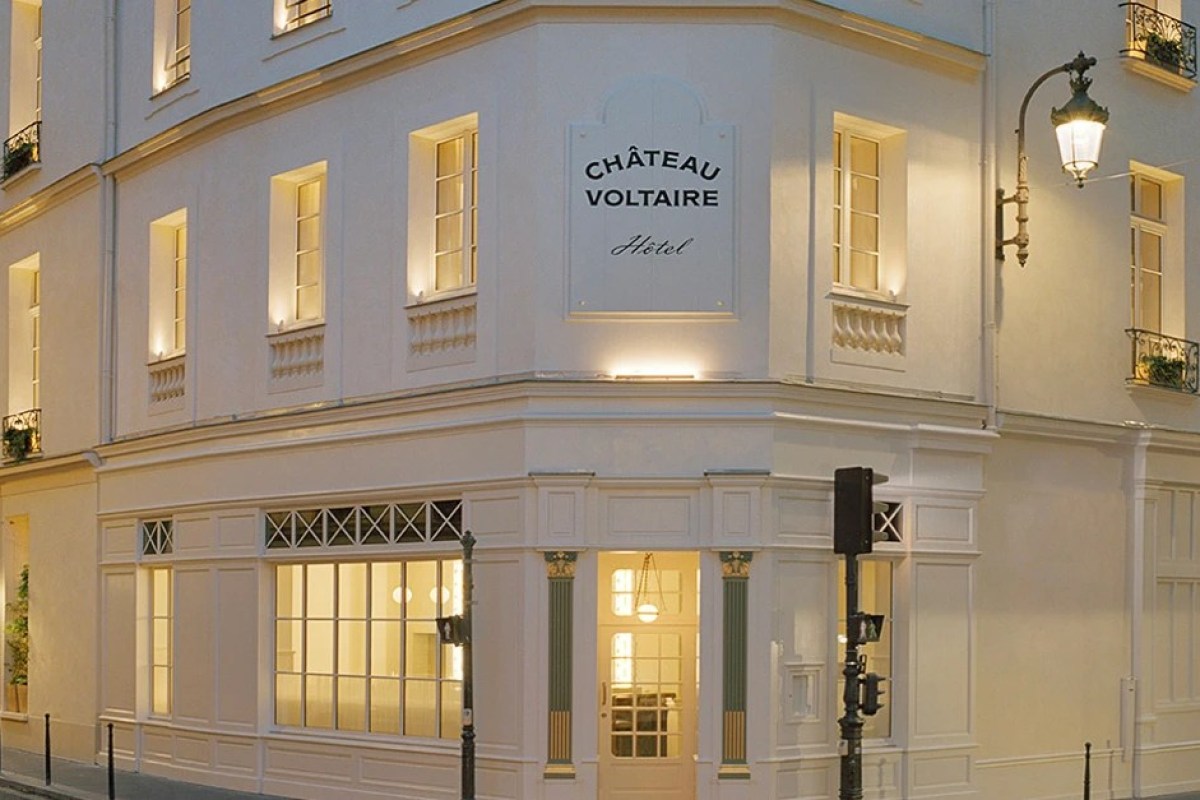 Château Voltaire hotel façade at dusk with illuminated sign and corner entrance