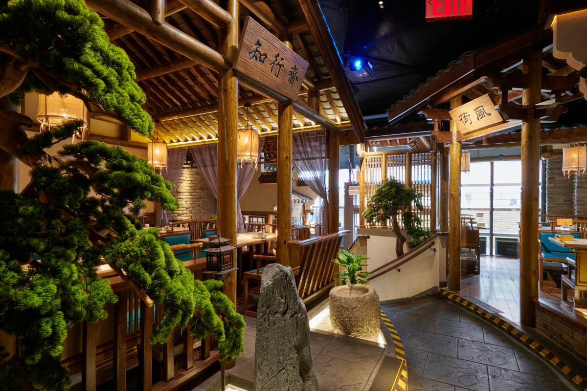 Restaurant interior with wooden pavilion architecture, bonsai trees, stone features and signage