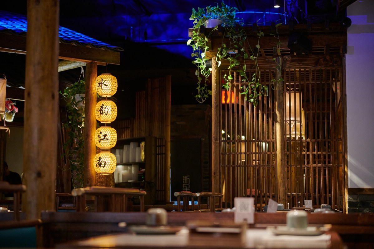 Dining room with wooden pavilion structure, glowing lanterns and hanging plants