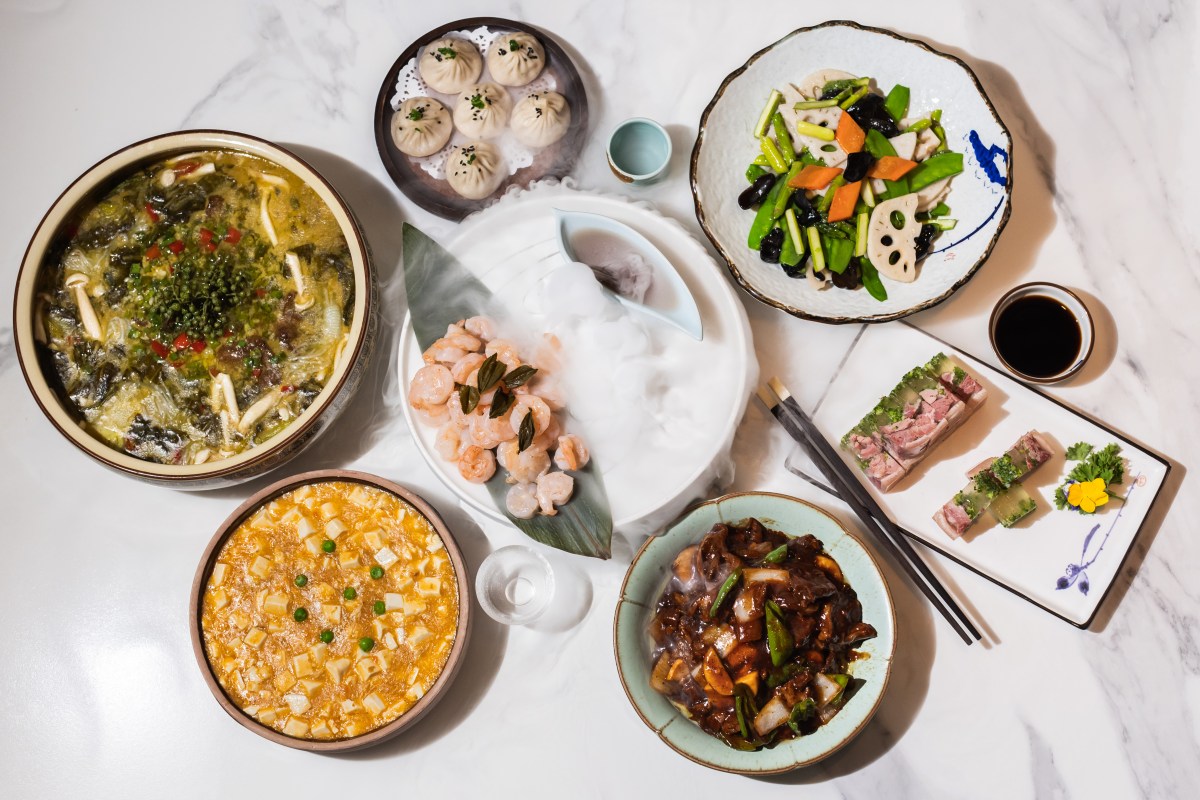 Overhead view of assorted Chinese dishes including dumplings, shrimp, tofu and vegetables on marble table