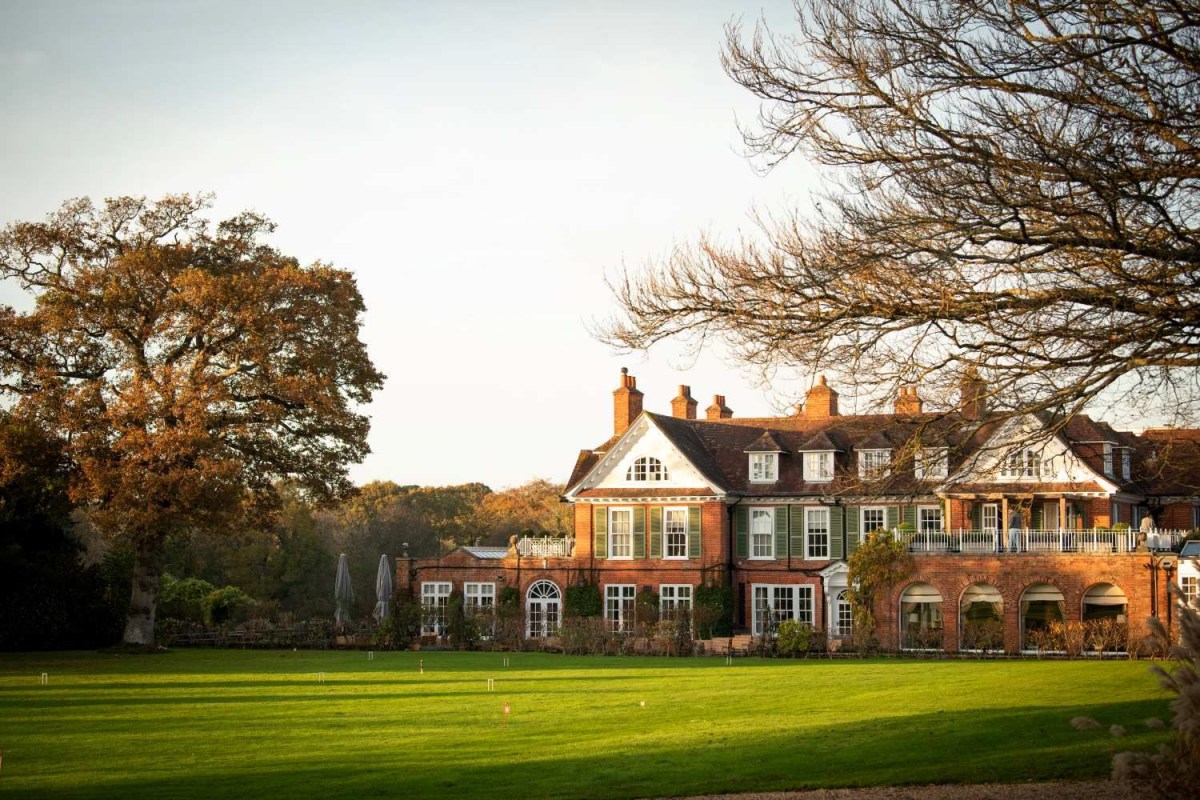 Red brick country house exterior seen across a lawn with autumn trees at golden hour