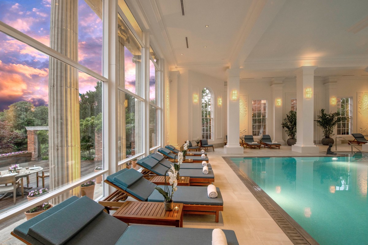 Indoor hotel swimming pool with loungers, classical columns and large windows at dusk