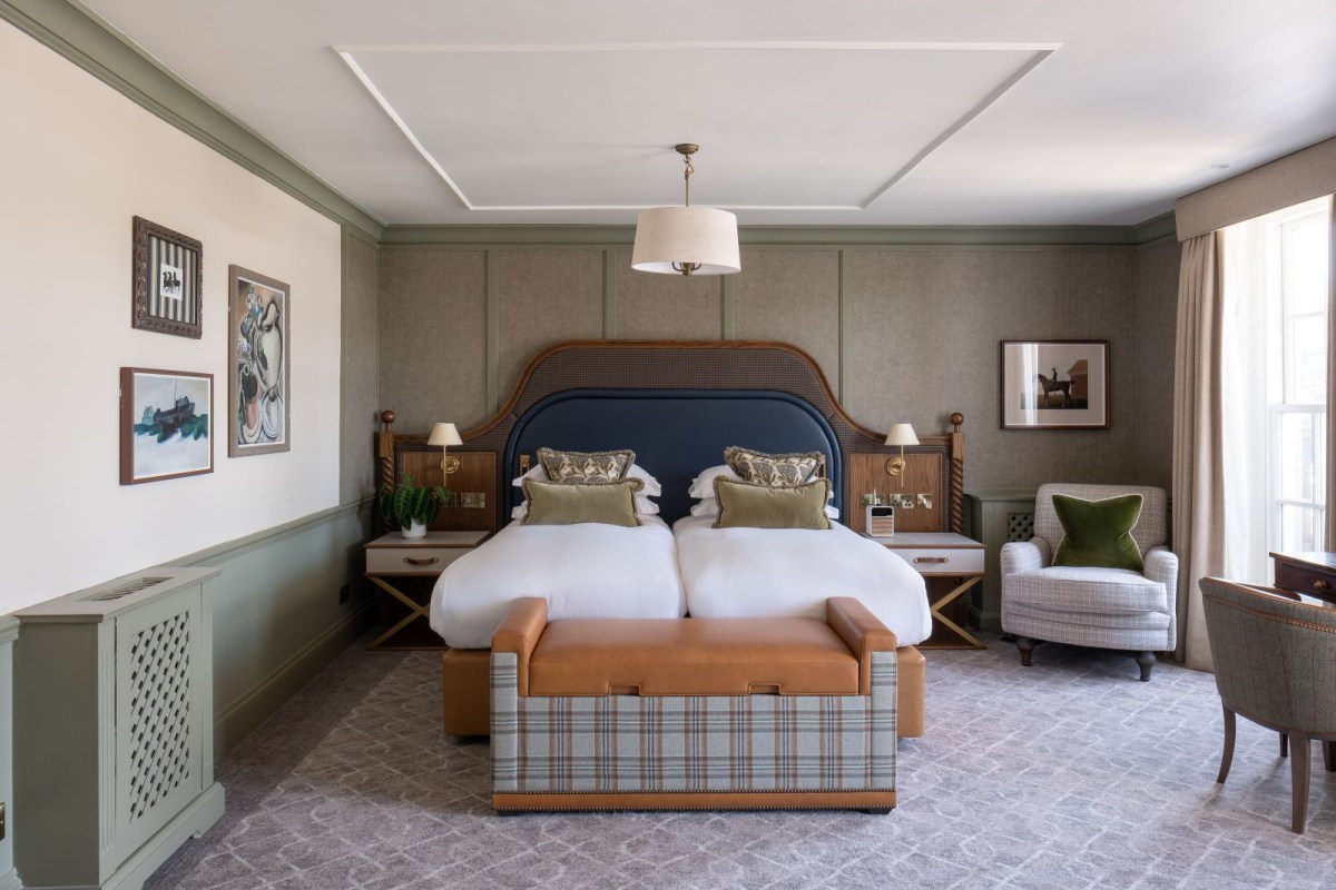 Hotel guest suite with twin beds, patterned headboard, armchair and framed art on walls
