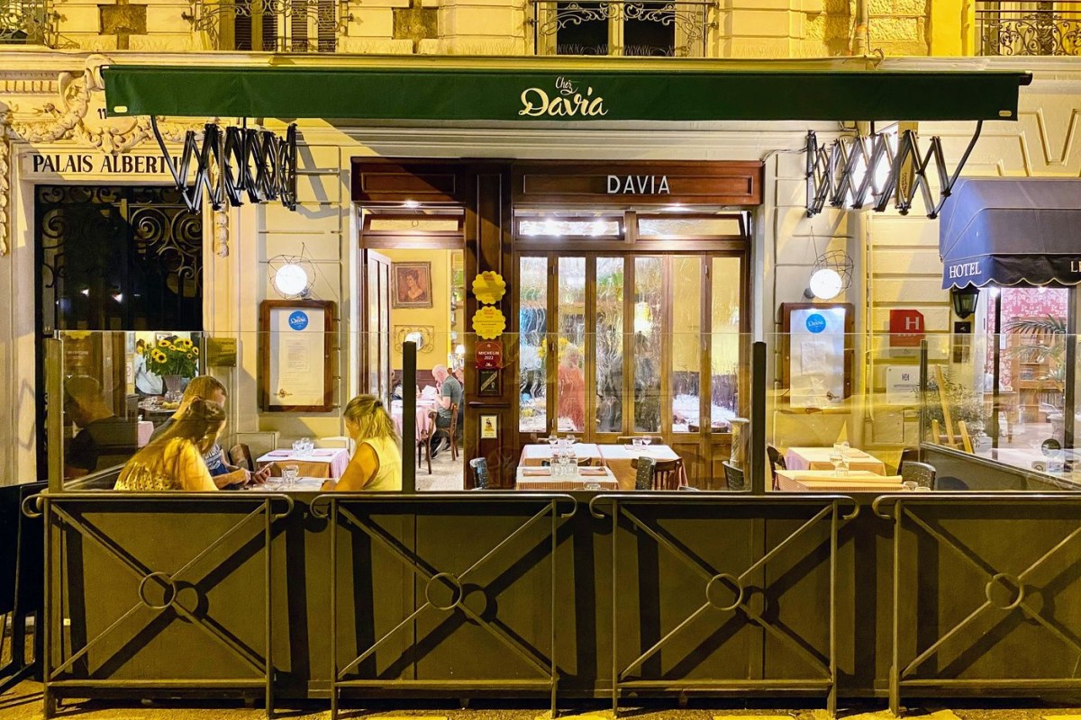 Chez Davia restaurant exterior at night with green awning, terrace tables and glass doors