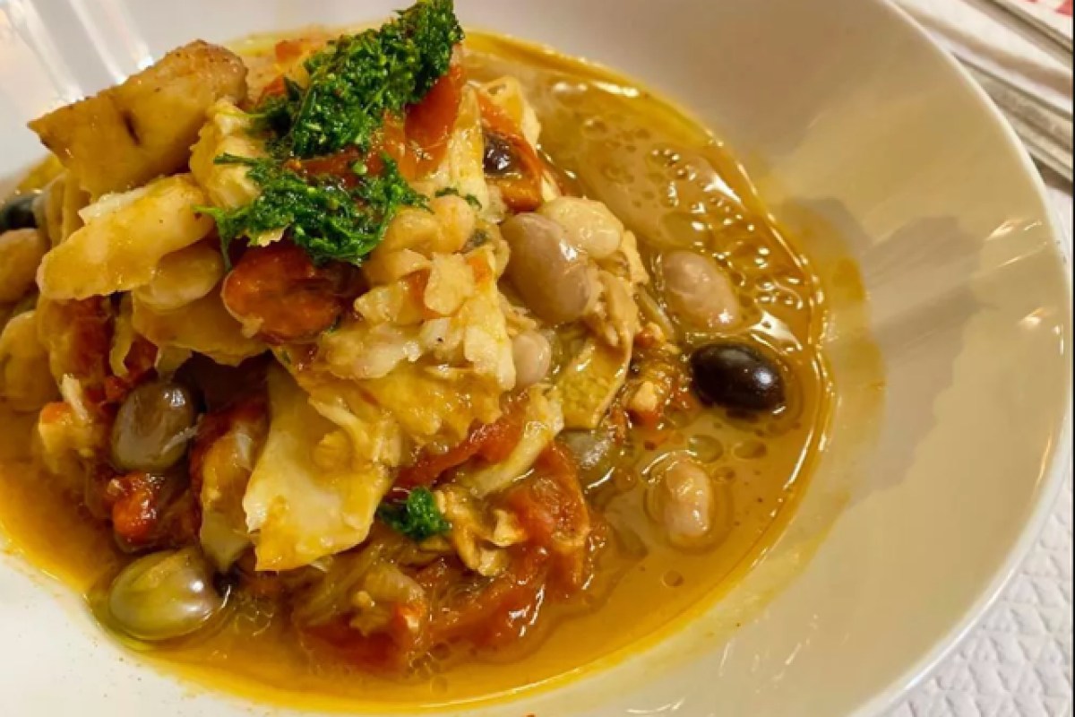 Bowl of fish stew with white beans, tomato sauce, olives and pesto garnish