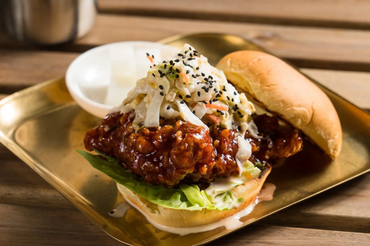 Fried chicken sandwich with coleslaw on a gold tray, wooden table background