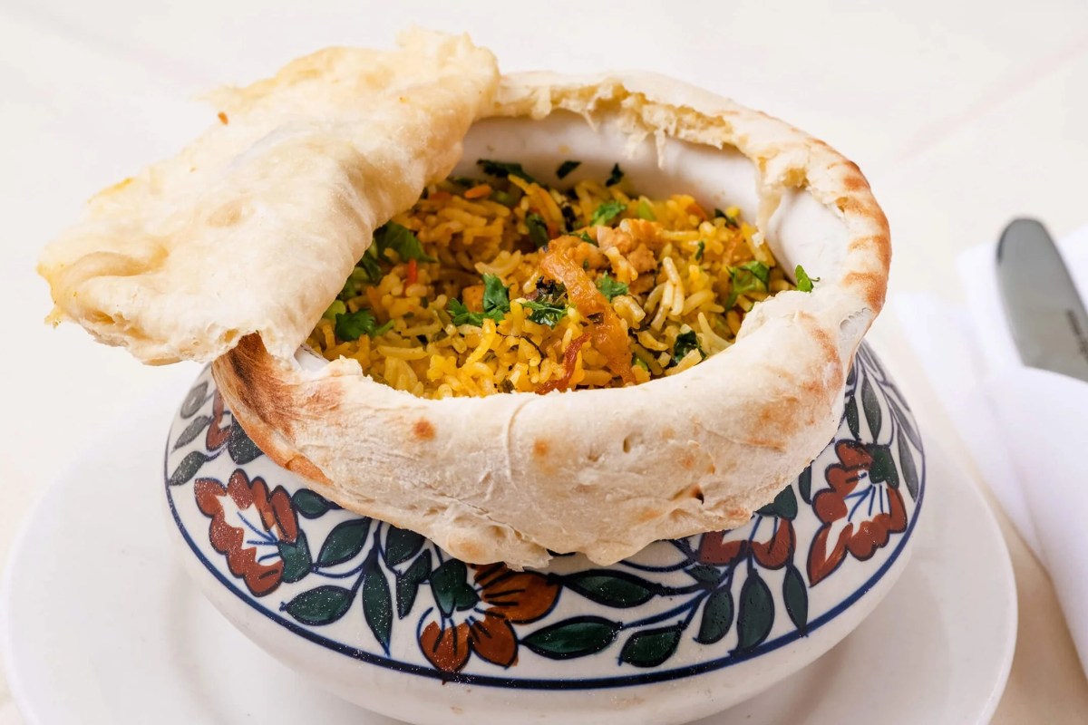 Biryani rice dish served inside a bread bowl with naan draped over the top