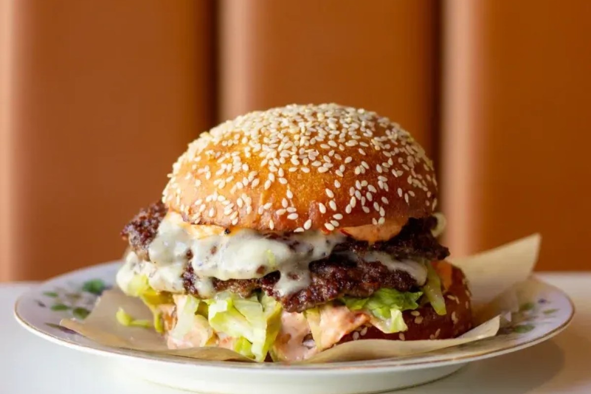 A sesame bun burger with melted cheese, meat patty, and lettuce on a plate