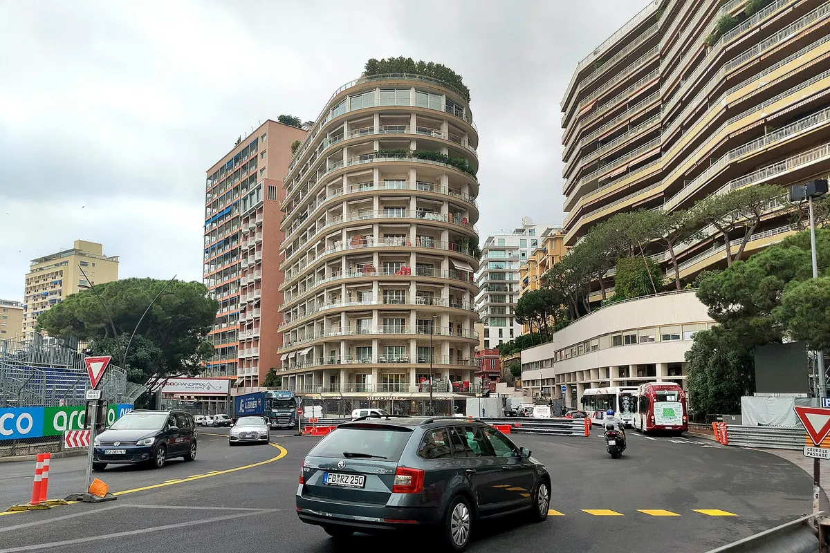 Everyday traffic at the Sainte-Dévote corner of the Circuit de Monaco, with red-and-white kerbs and curved apartment towers