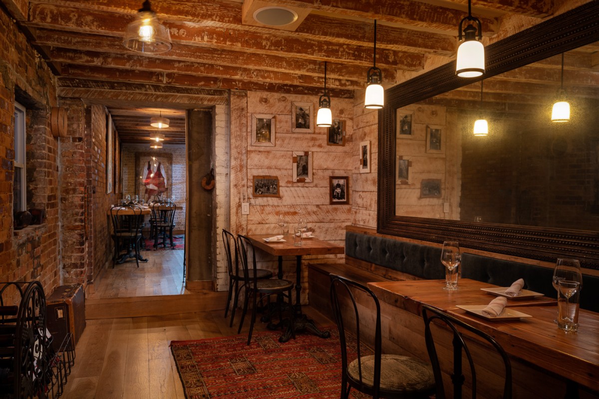 Cozy dining room with exposed brick, wood beams, framed photos, and set tables leading to another room
