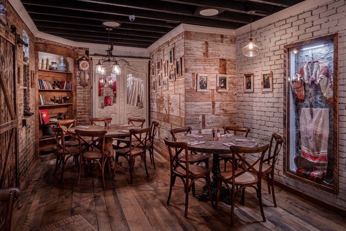 Rustic dining room with white brick walls, wooden tables and chairs, framed photos, and traditional costume display