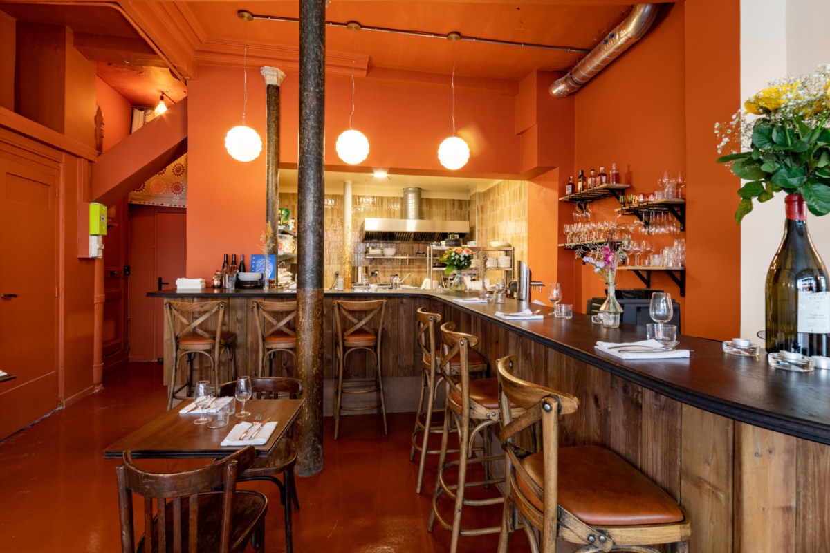 Interior of Clutch restaurant showing orange-walled dining room with wooden bar, stools, open kitchen, and hanging globe lights