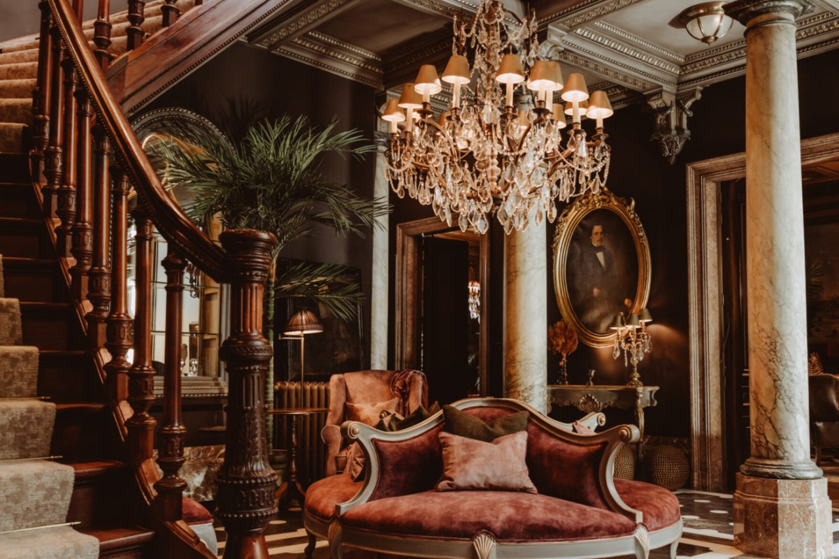Grand hotel lobby with marble columns, chandelier, antique staircase, and vintage portrait