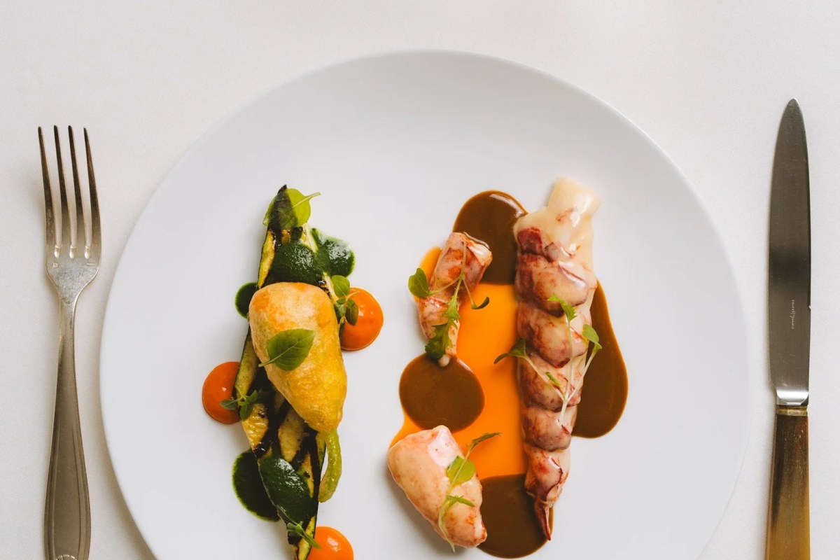 Plated lobster and vegetable dish with sauce, flanked by fork and knife